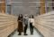 Three students browsing a card catalog aisle in a modern library setting.