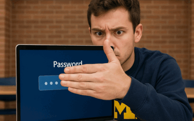 A U-M student looking concerned covers his password with his hand on his laptop.