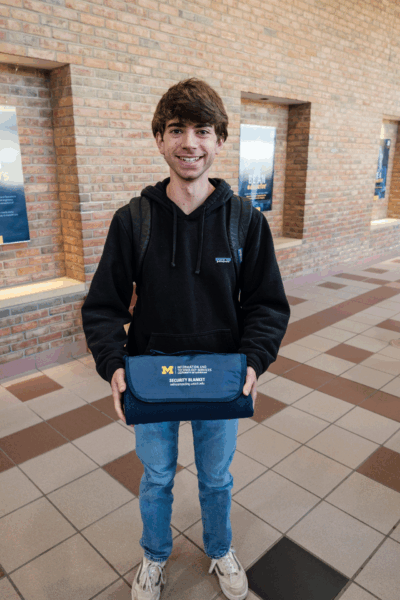 A U-M student holding an ITS Information Assurance Security Blanket that they won playing Plinko at a Safe Computing pop up table.