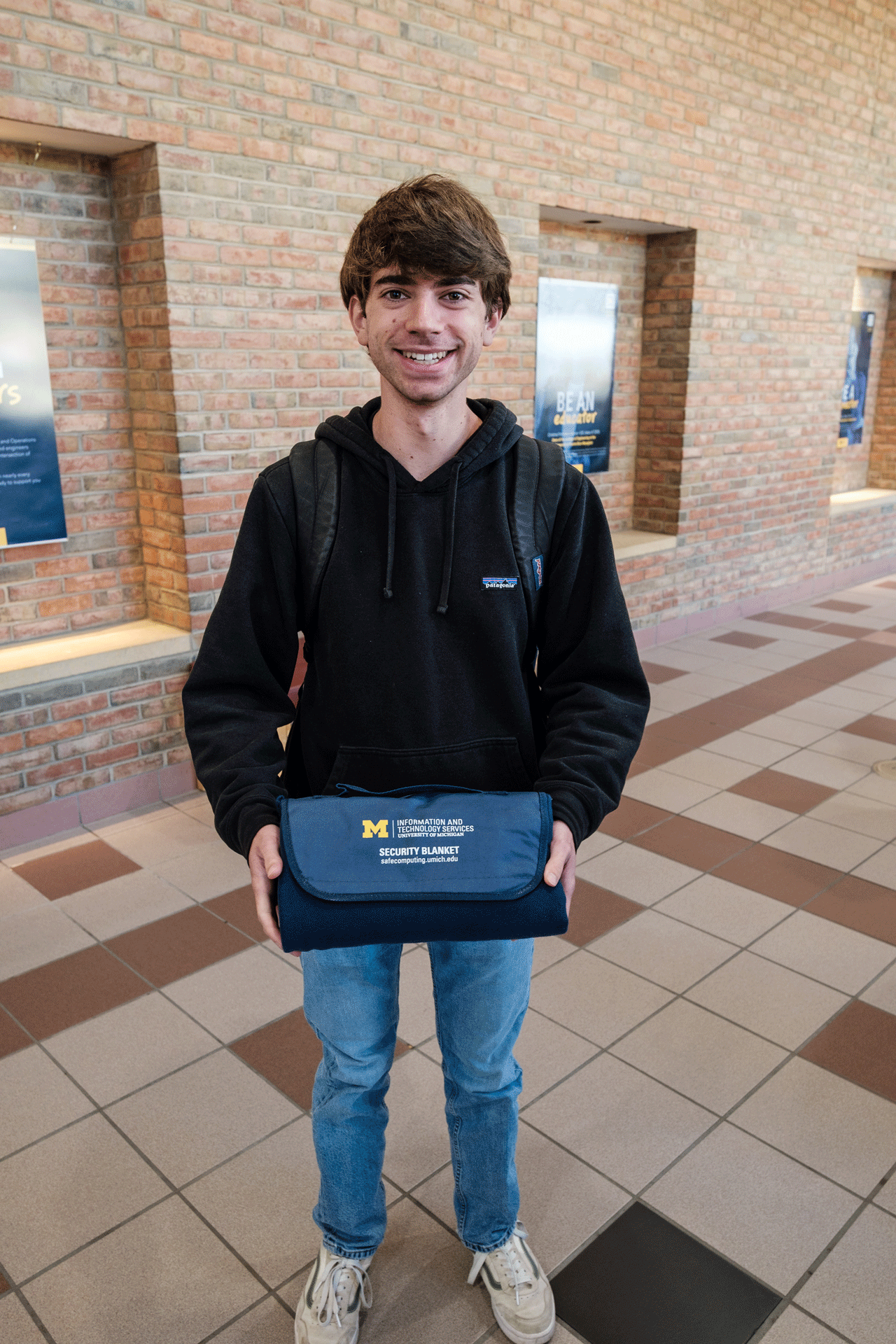 A U-M student holding an ITS Information Assurance Security Blanket that they won playing Plinko at a Safe Computing pop up table.