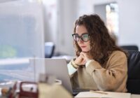 Young, serious, busy, professional, business woman, employee, or student using laptop watching online webinar or training web course, looking at computer, thinking,