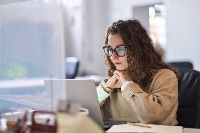Young, serious, busy, professional, business woman, employee, or student using laptop watching online webinar or training web course, looking at computer, thinking,